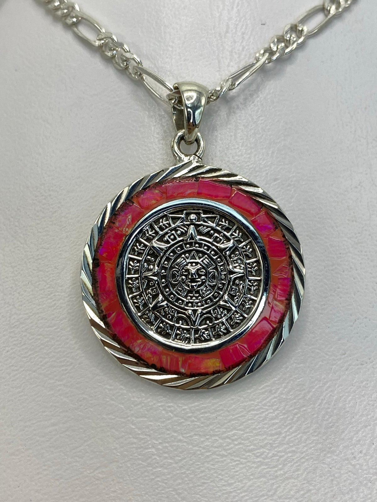 Dije de plata .950 con Calendario Azteca en relieve y ópalo de fuego rosa en el centro, colgado de cadena de plata
