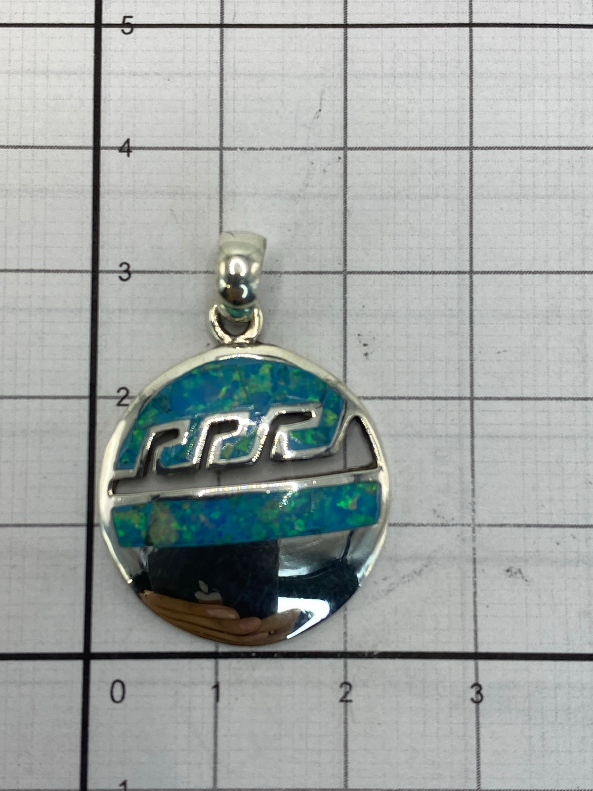 Dije sobre paño azul, midiendo 3 × 2 cm en escala