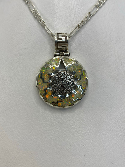Vista frontal del dije: calendario azteca en relieve con detalles de glifos y ópalo de fuego en el centro