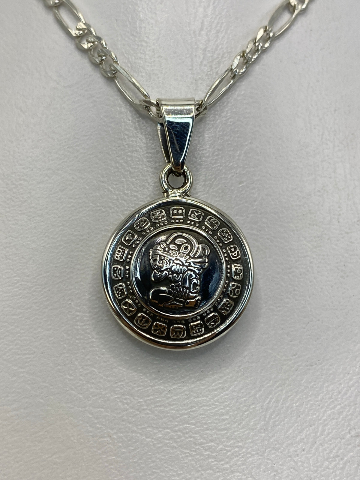 Dije de plata con calendario azteca prehispánico, 2.8 cm de largo, colgando sobre fondo blanco