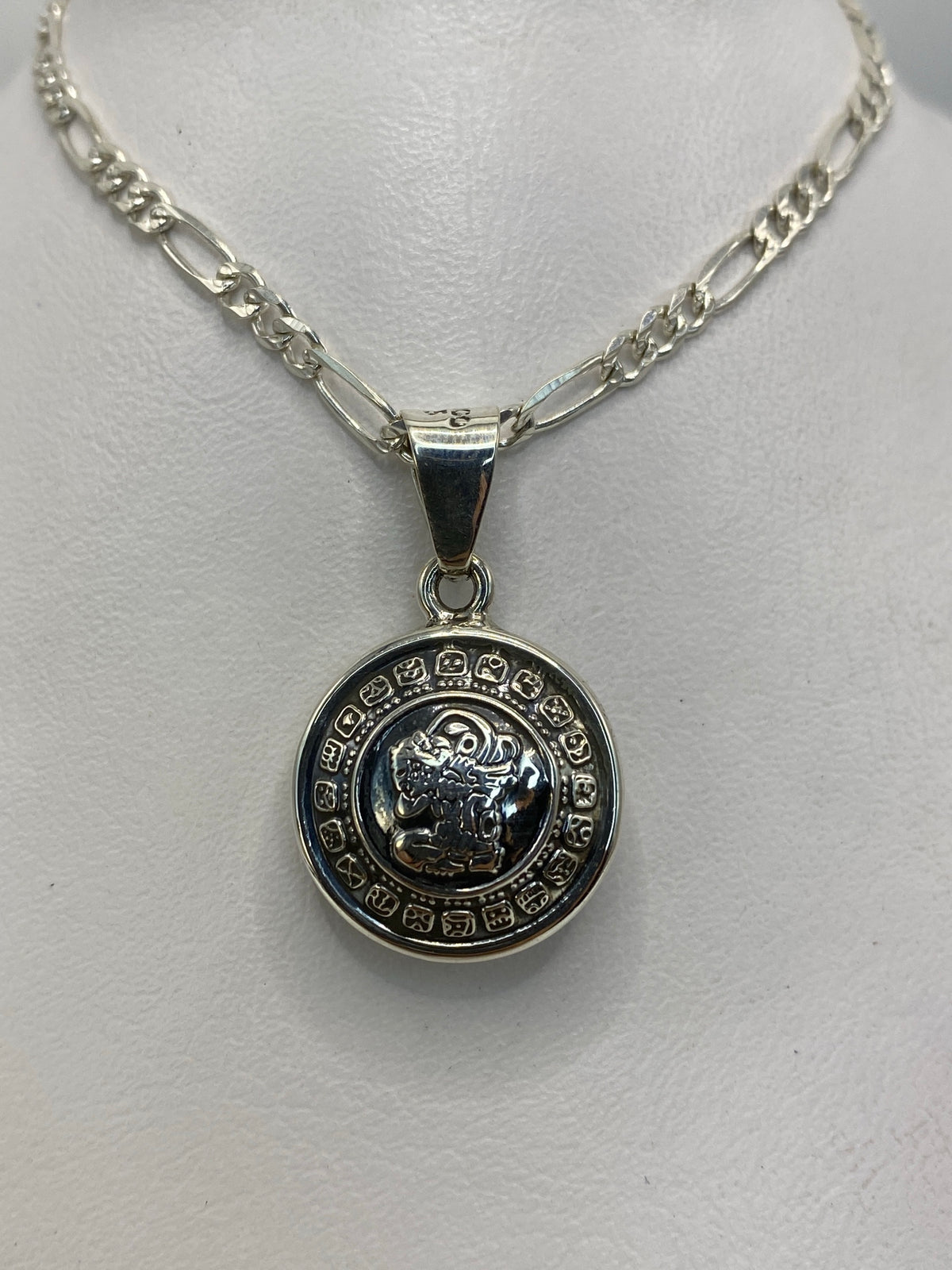 Detalle frontal del dije redondo con glifos grabados y figura central azteca en plata