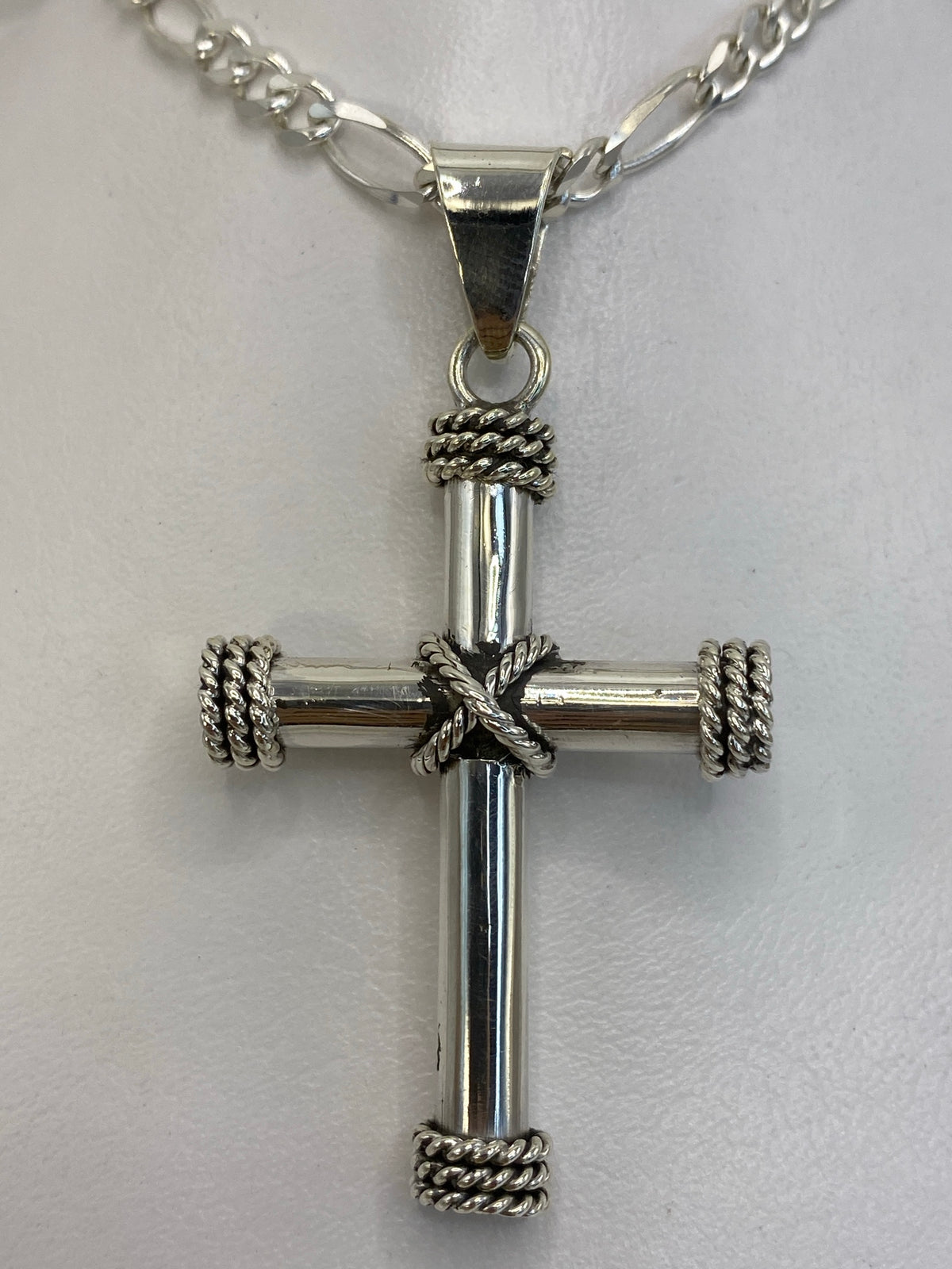 Dije cruz de plata 925 colgando de una cadena figaro, vista frontal