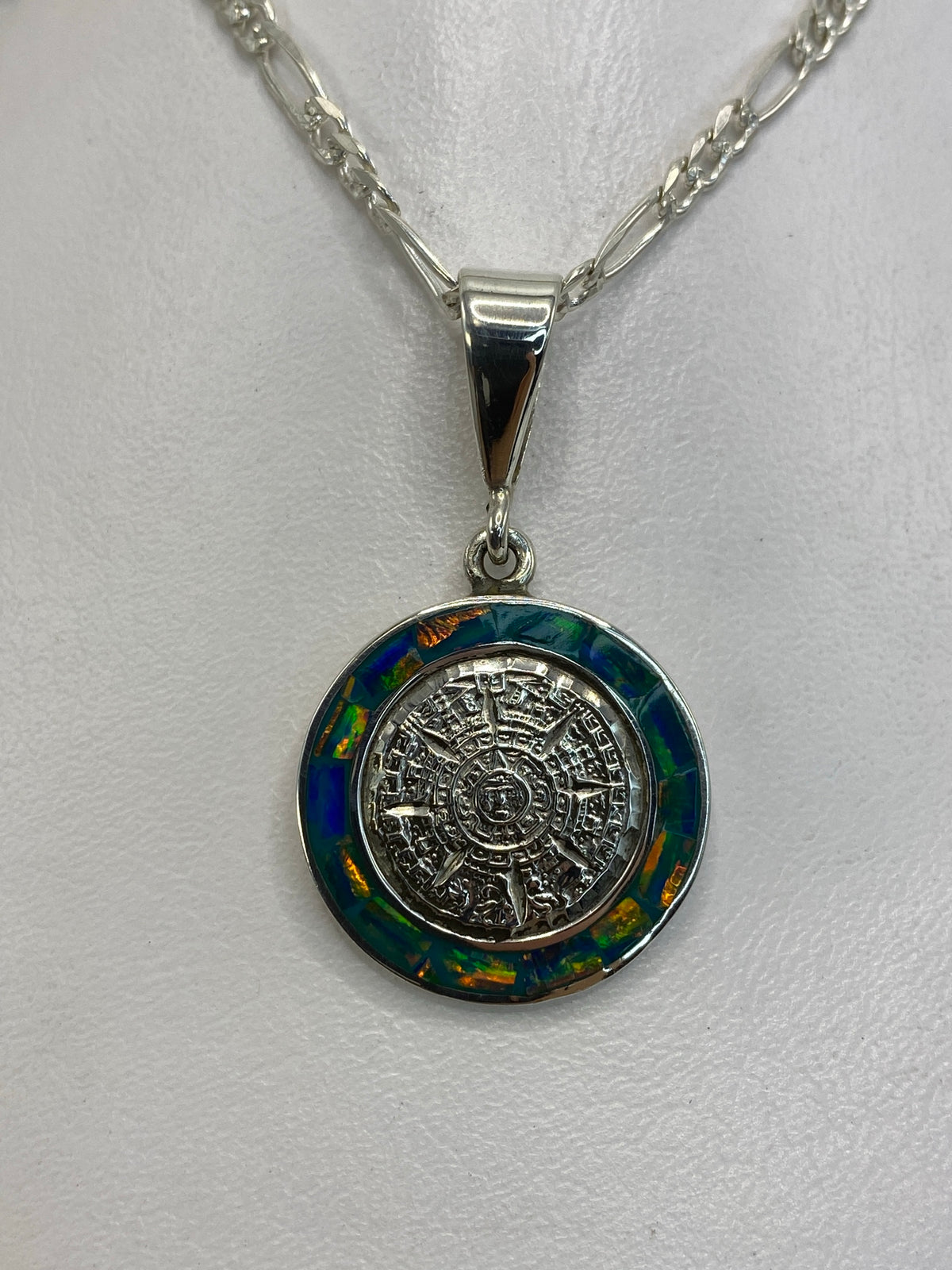 Dije Calendario Azteca de plata 950 con Ópalo de Fuego azul, colgante en cadena de eslabones sobre fondo blanco