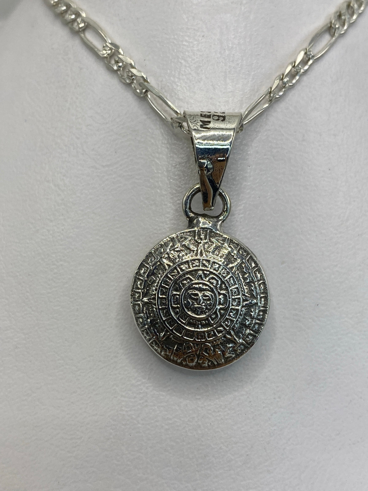Dije de plata con calendario azteca en relieve, visto de frente sobre fondo blanco