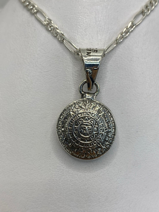 Dije de plata con calendario azteca en relieve, visto de frente sobre fondo blanco
