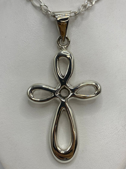 Cruz de plata sobre regla métrica midiendo 7 cm de largo y 3.5 cm de ancho