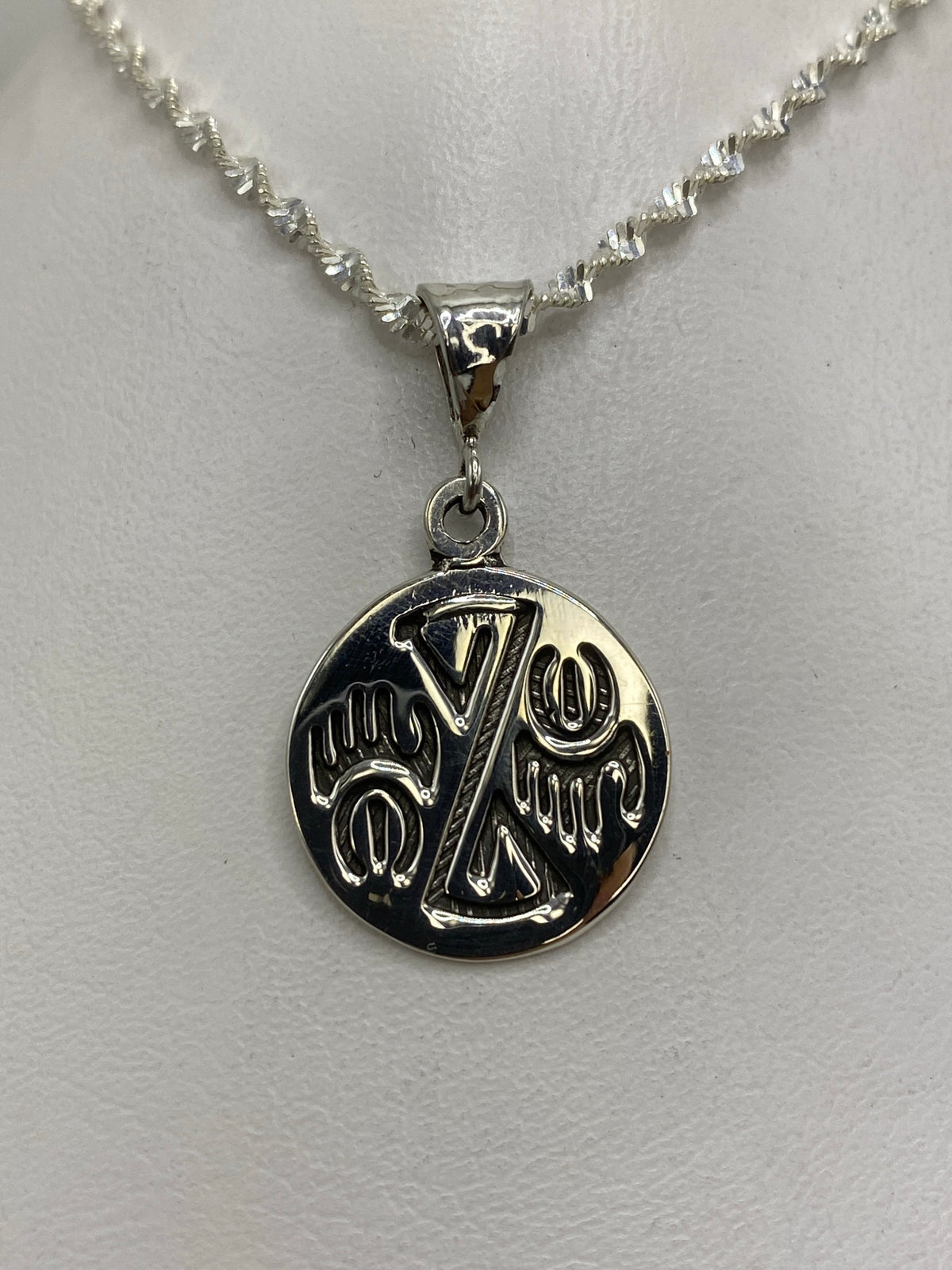 Dije de plata con diseño de sello prehispánico en relieve, colgado de cadena