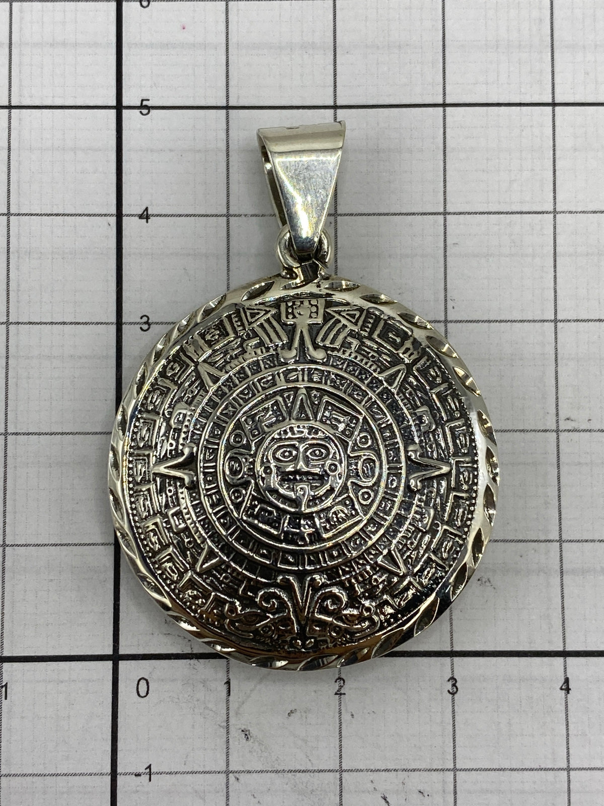 Dije del Calendario Azteca sobre medidor de referencia — 5 cm de largo × 3.5 cm de ancho