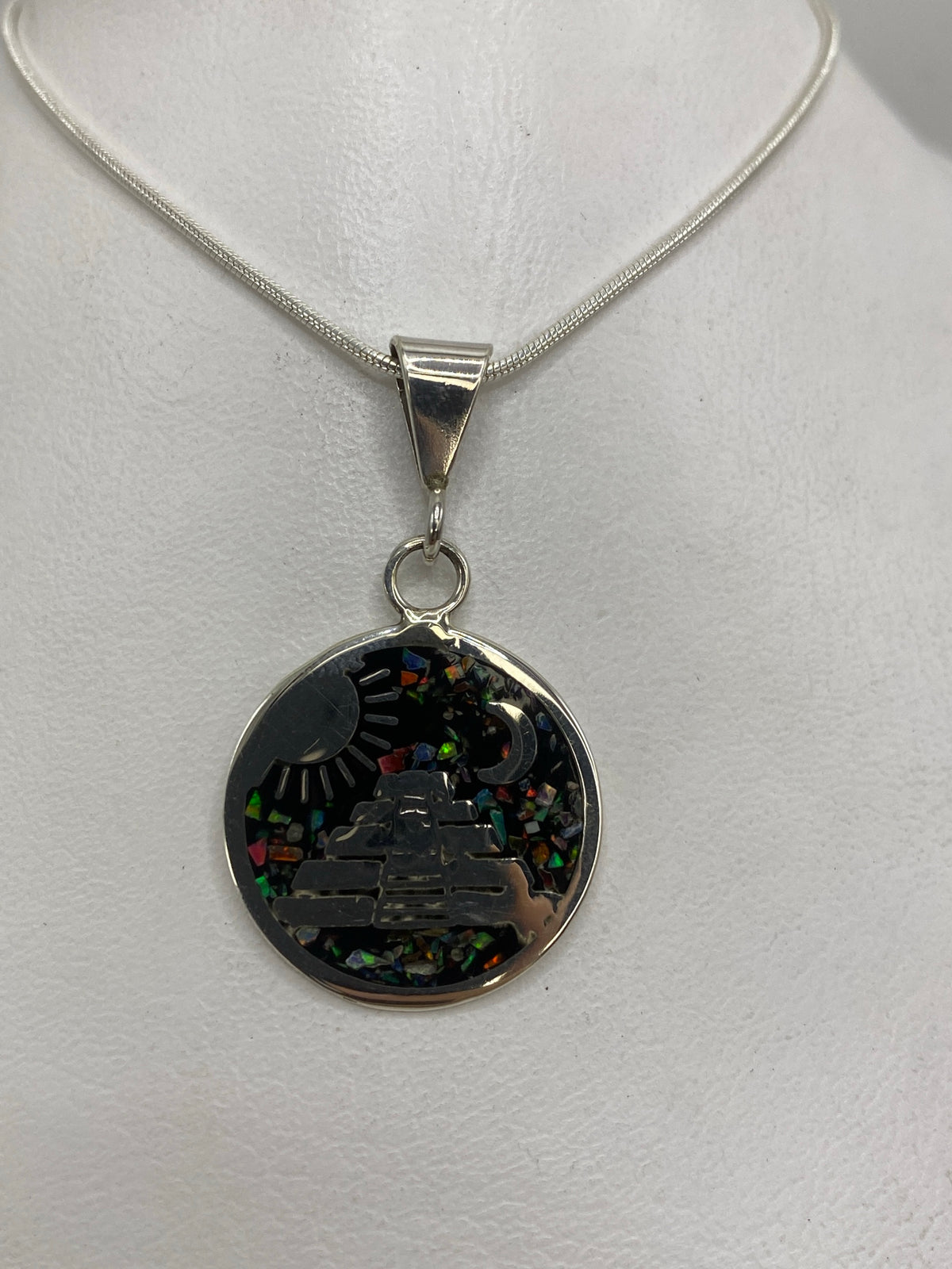 Detalle del dije mostrando la pirámide escalonada, símbolos de sol y luna, y los colores del ópal de fuego