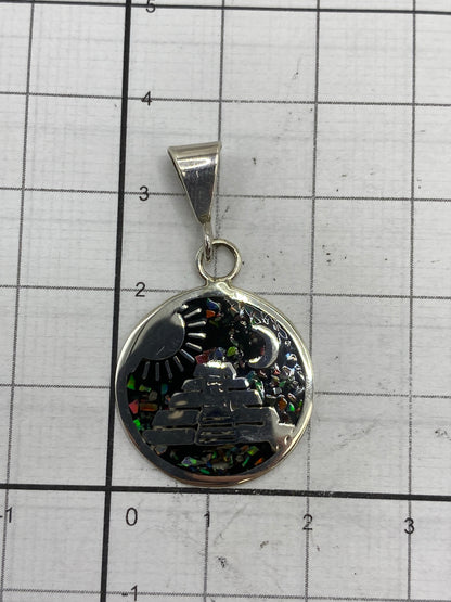 Dije de tamaño comparativo (3.5 × 2 cm) en mano, mostrando cómo cuelga puesto