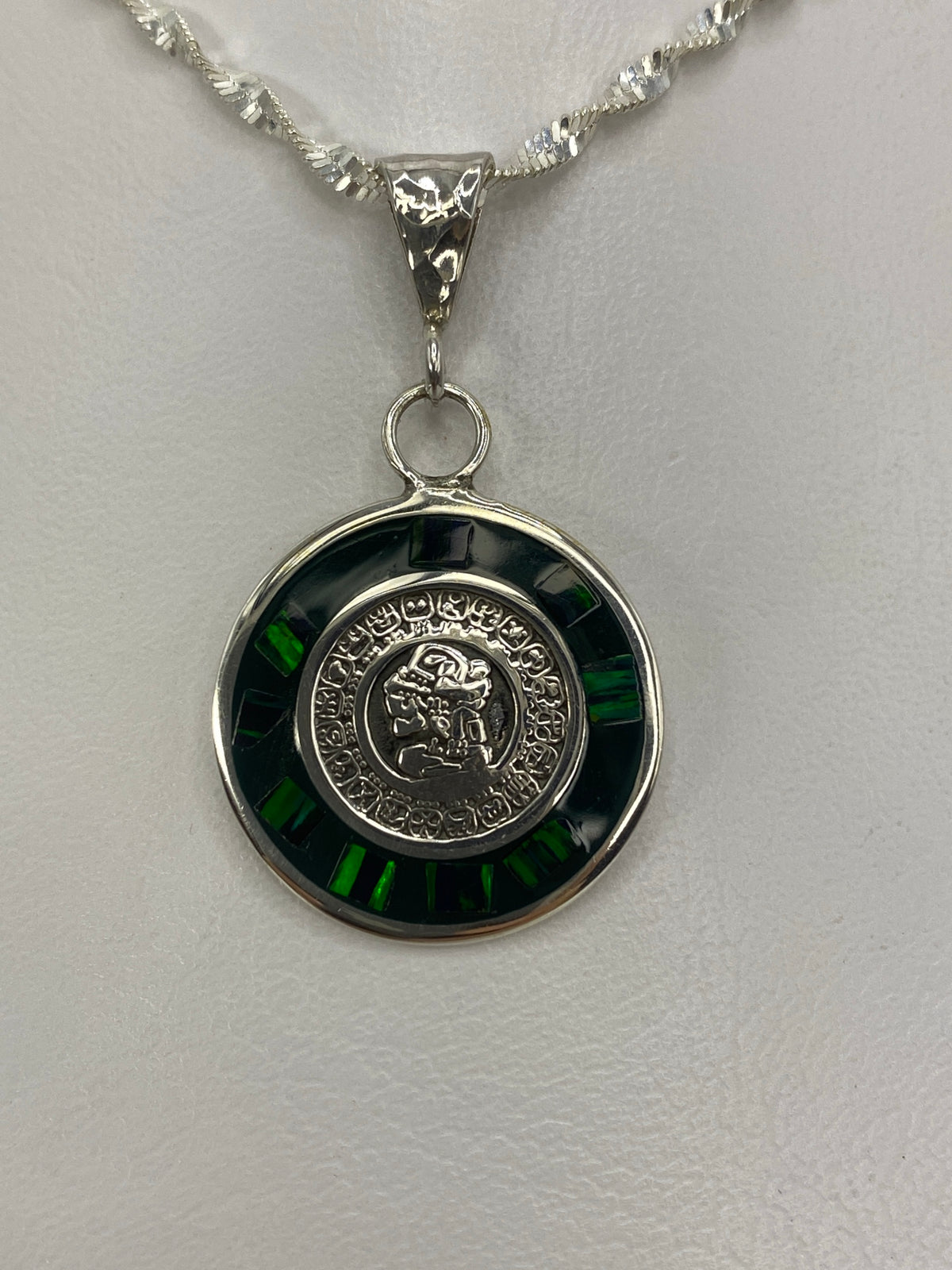 Dije de plata con calendario azteca y ópalo de fuego verde, colgando de cadena de plata retorcida