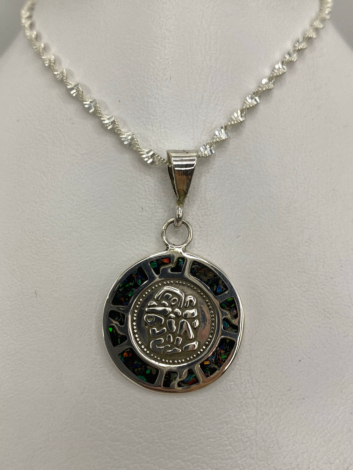 Detalle frontal del dije mostrando el ópalo multicolor (azul, verde, naranja) en engaste de plata