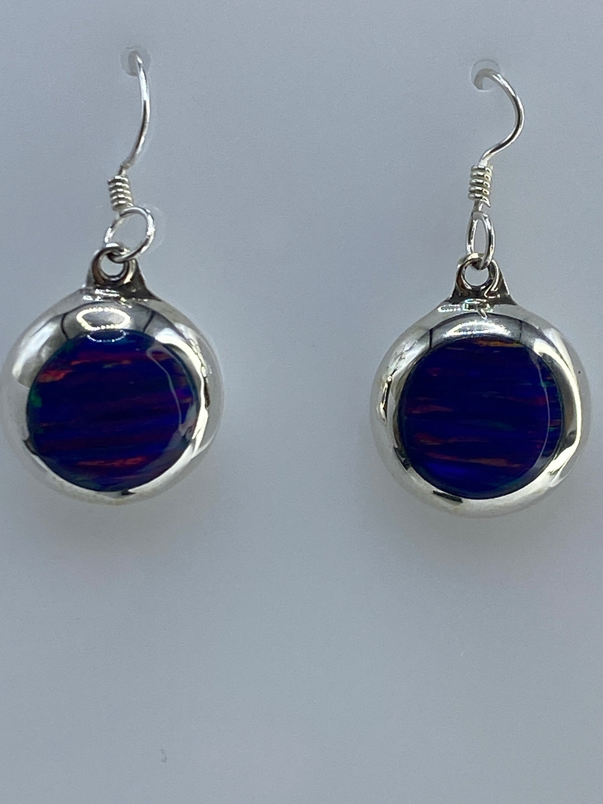 Par de aretes de plata 925 con ópalo de fuego azul, colgando sobre fondo gris