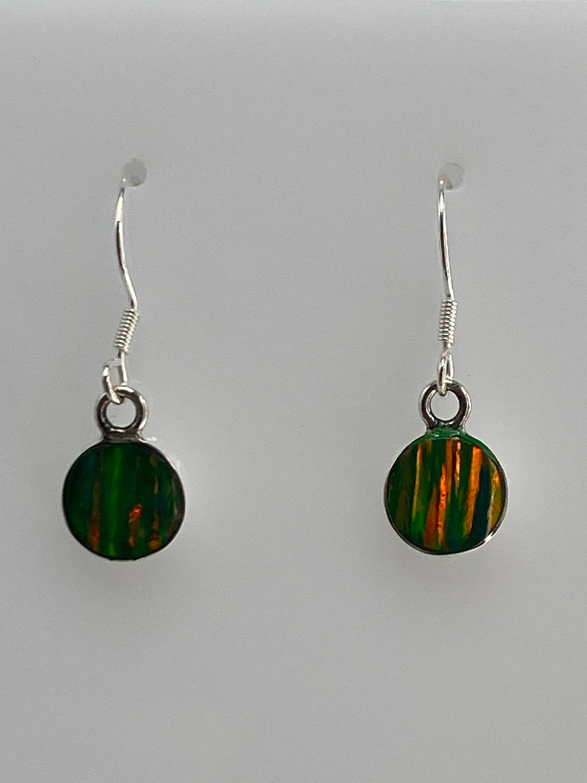 Vista frontal de los aretes mostrando el color verde del ópalo con destellos cálidos