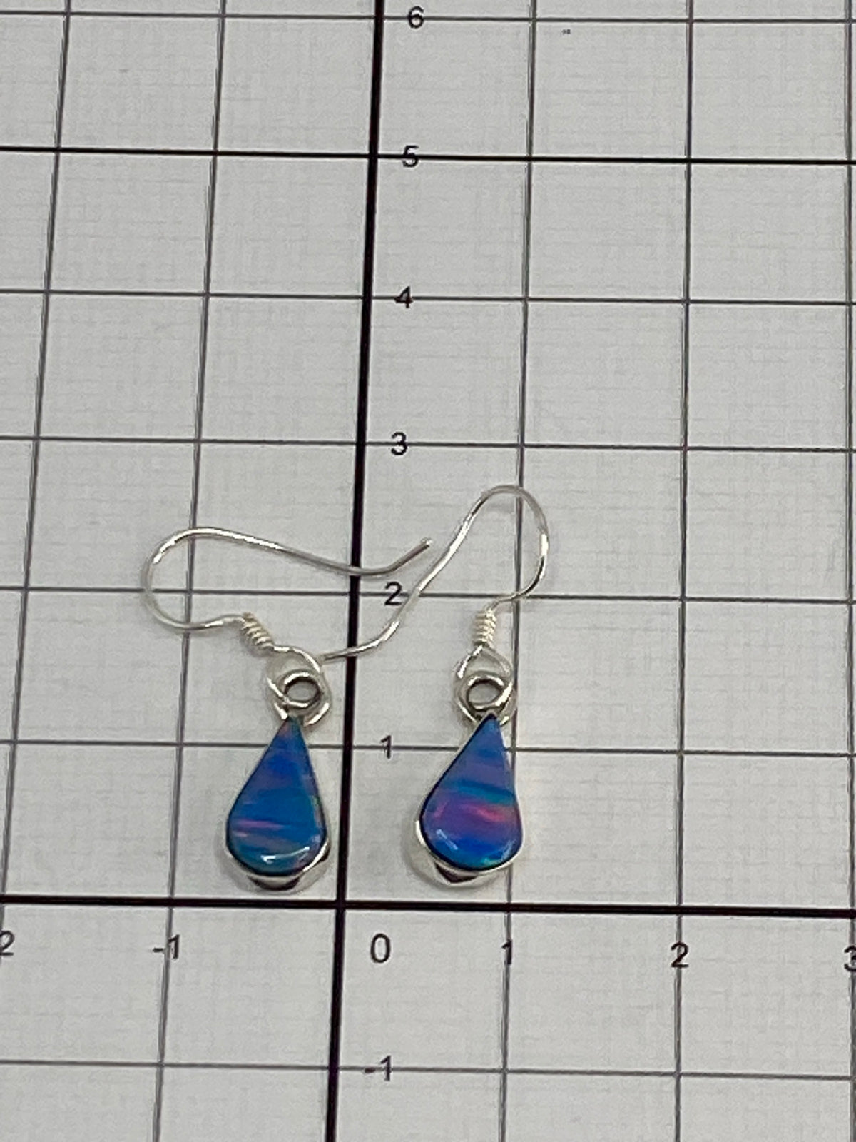 Aretes en la mano con fondo blanco, mostrando el tamaño de 2 cm de largo