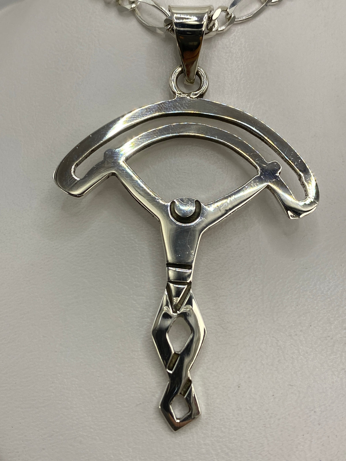 Dije de plata calado en forma de dos arcos simétricos, 6.7 cm de largo, sobre fondo blanco