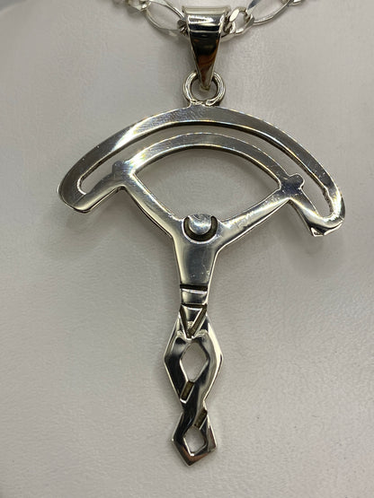 Dije de plata calado en forma de dos arcos simétricos, 6.7 cm de largo, sobre fondo blanco