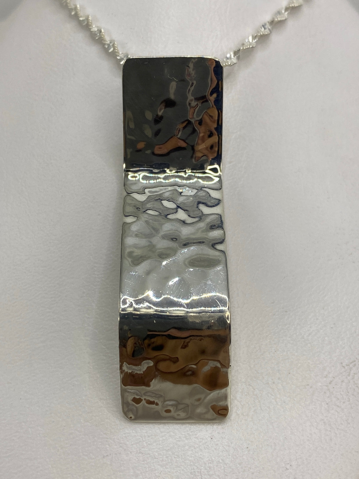 Dije de plata repujado alargado, 5.5 cm, con textura martillada en la mano