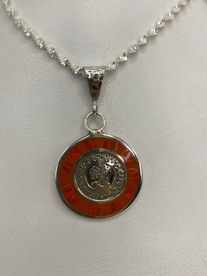 Vista frontal del dije de plata: moneda prehispánica rodeada de ópalo naranja