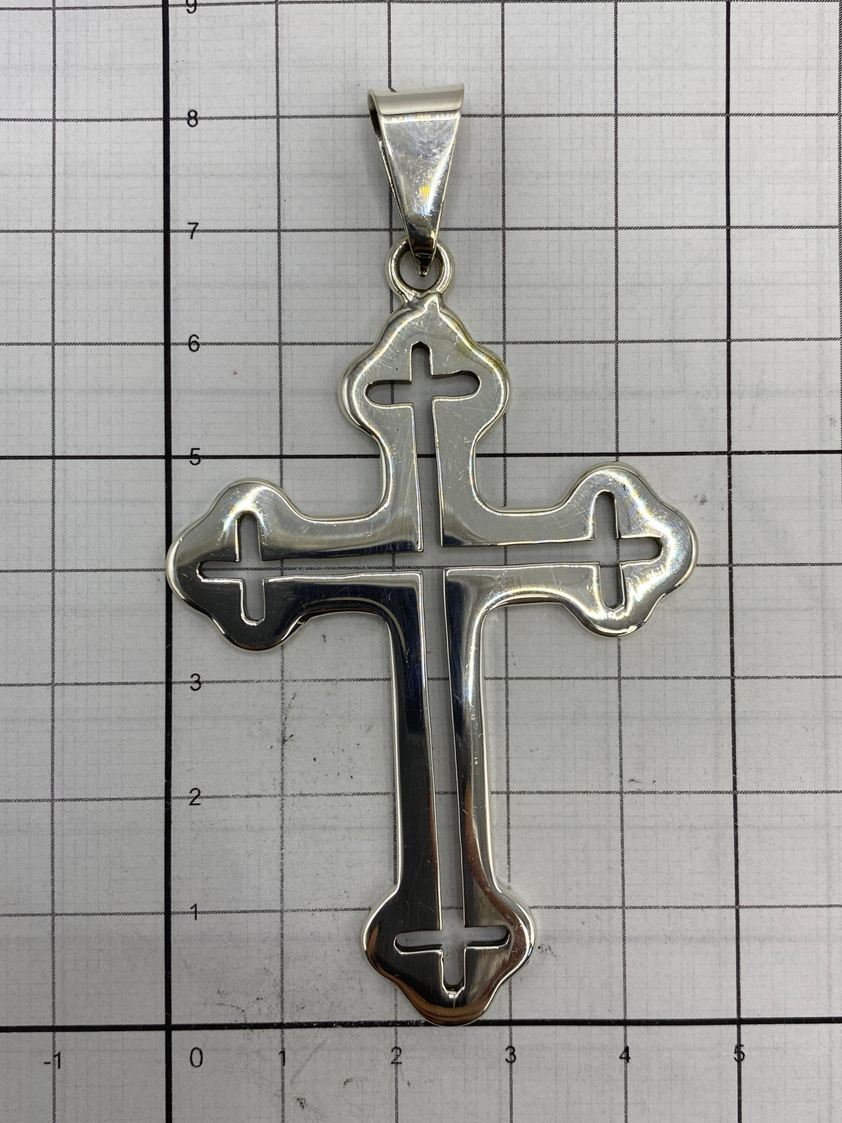 Dije cruz sobre regla métrica mostrando sus dimensiones exactas de 8.2 × 4.7 cm