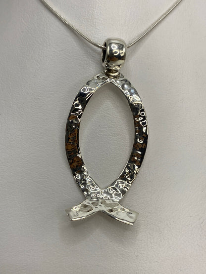 Dije de plata 925 en repujado con diseño de sello prehispánico, colgando de una cadena plateada