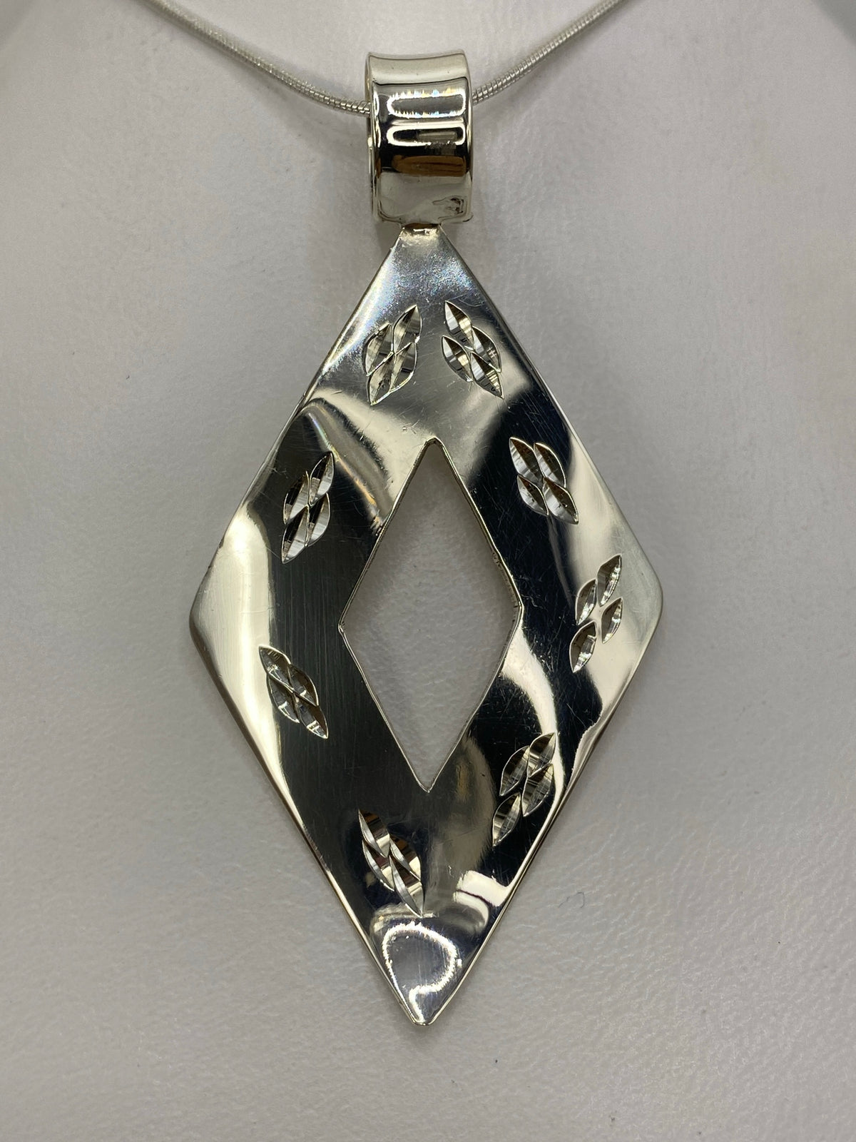 Dije de plata 925 con forma de rombo geométrico calado, colgando de una cadena de plata
