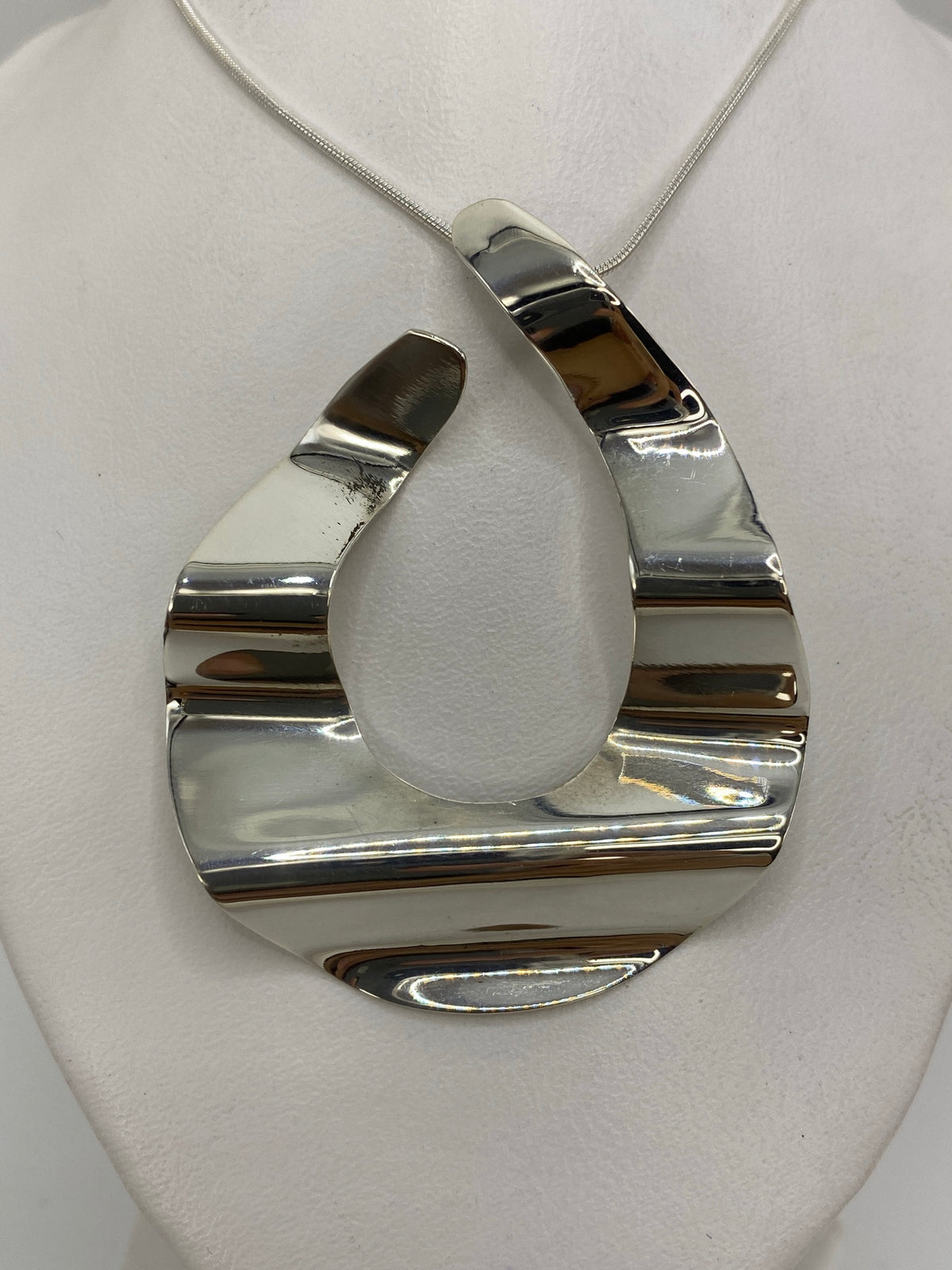 Dije de plata geométrico 3D visto de frente sobre tela blanca