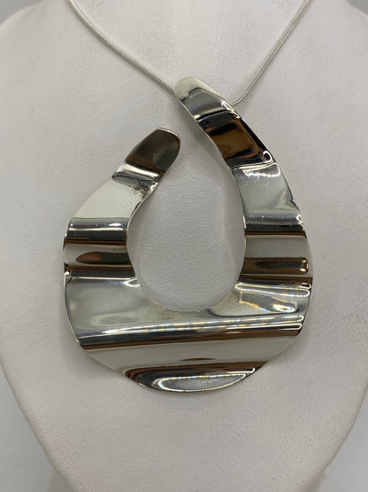 Dije de plata geométrico 3D visto de frente sobre tela blanca