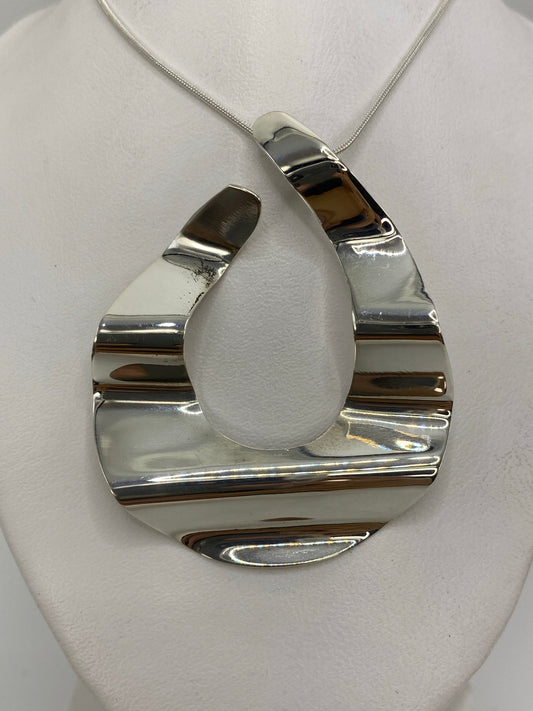 Dije de plata geométrico 3D visto de frente sobre tela blanca