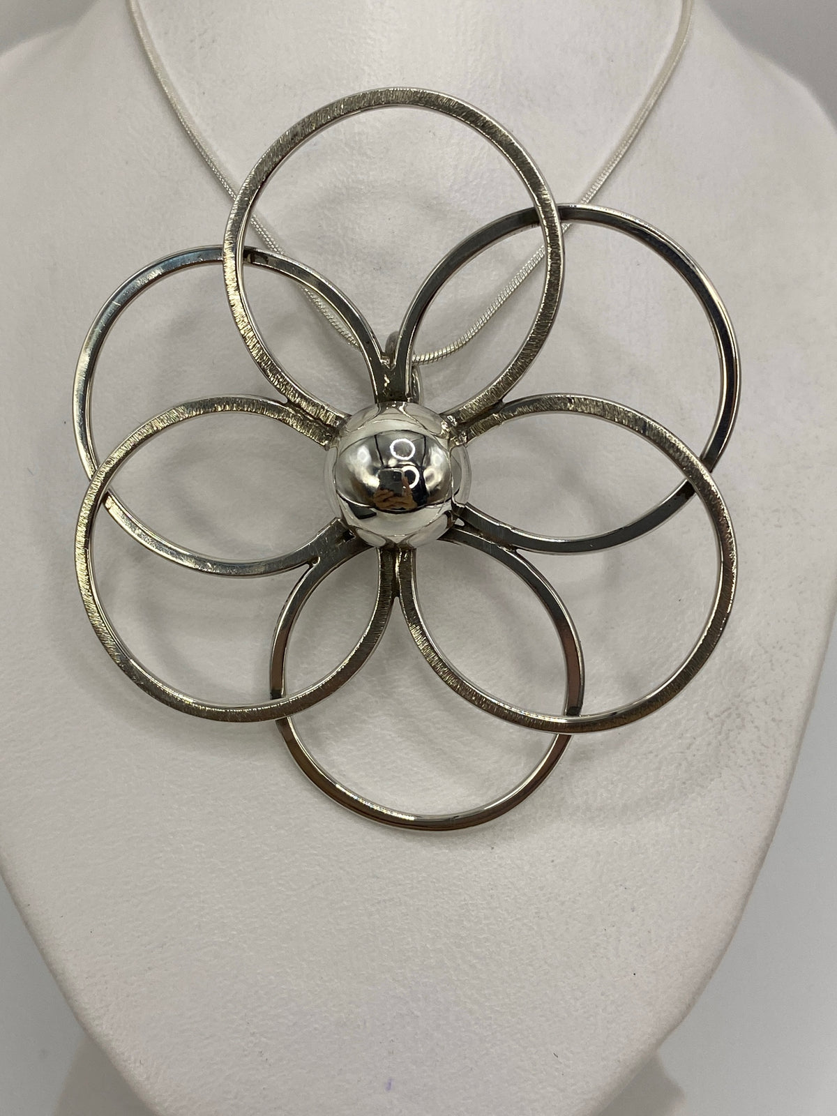 Dije floral de plata 925 con cinco pétalos en diseño geométrico, puesto sobre pecho