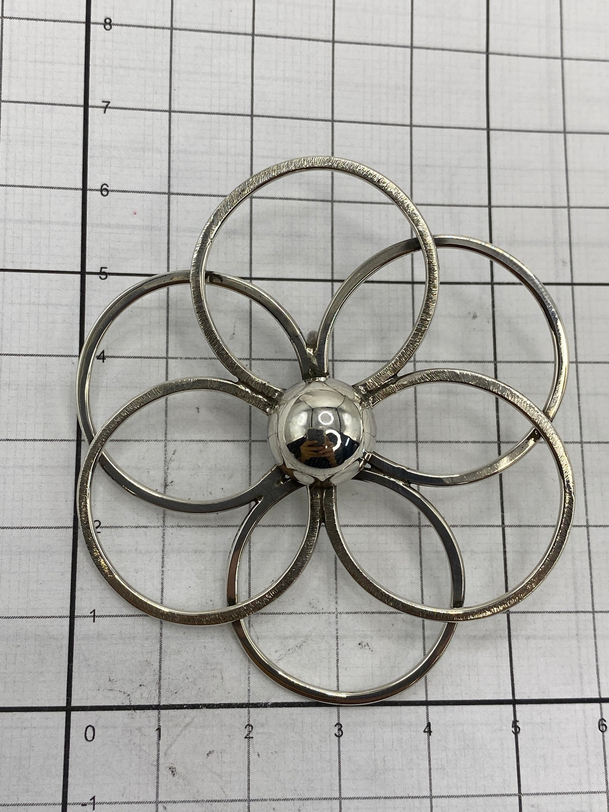 Dije floral sobre escala mostrando 6.1 × 5.5 cm de medidas reales