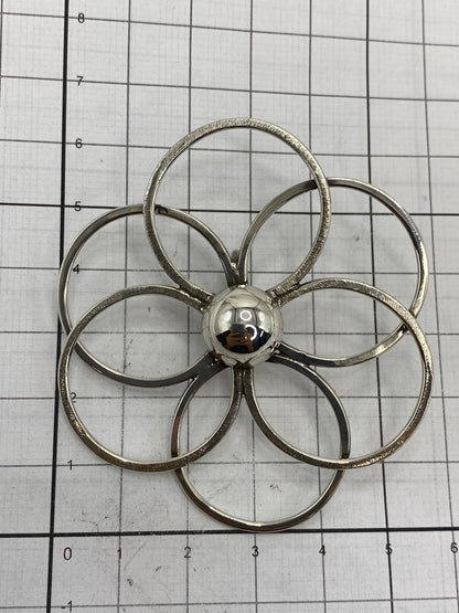 Dije floral sobre escala mostrando 6.1 × 5.5 cm de medidas reales