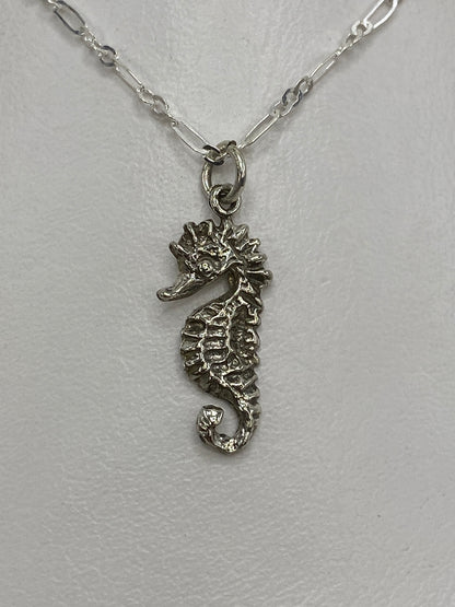 Dije de plata caballito de mar en repujado, visto de frente sobre fondo blanco