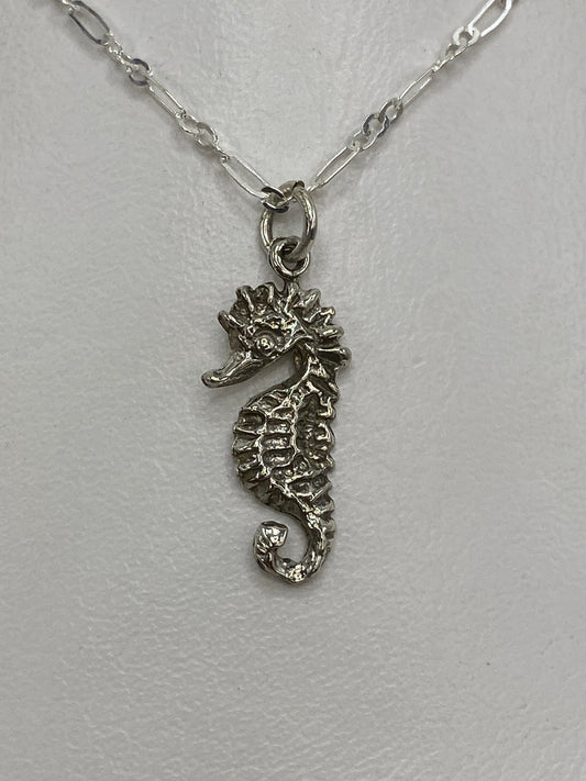 Dije de plata caballito de mar en repujado, visto de frente sobre fondo blanco