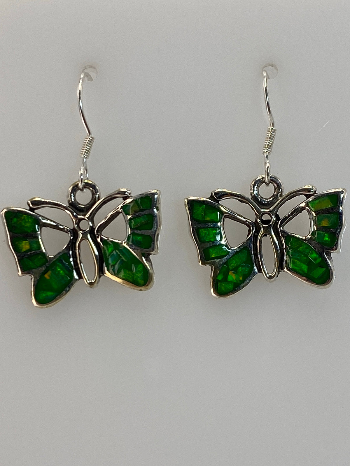 Par de aretes de plata 950 con ópalo de fuego verde, colgando del gancho, viendo la iridiscencia natural de la piedra