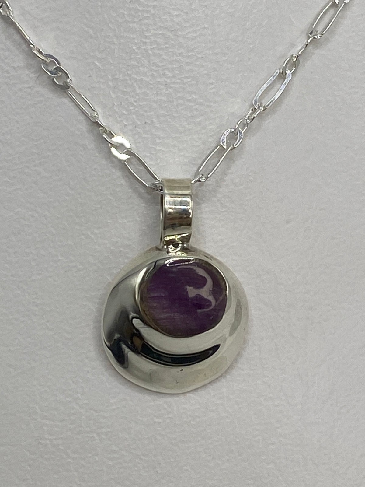 Dije de plata 925 con piedra morada engastada, colgando de cadena en el cuello