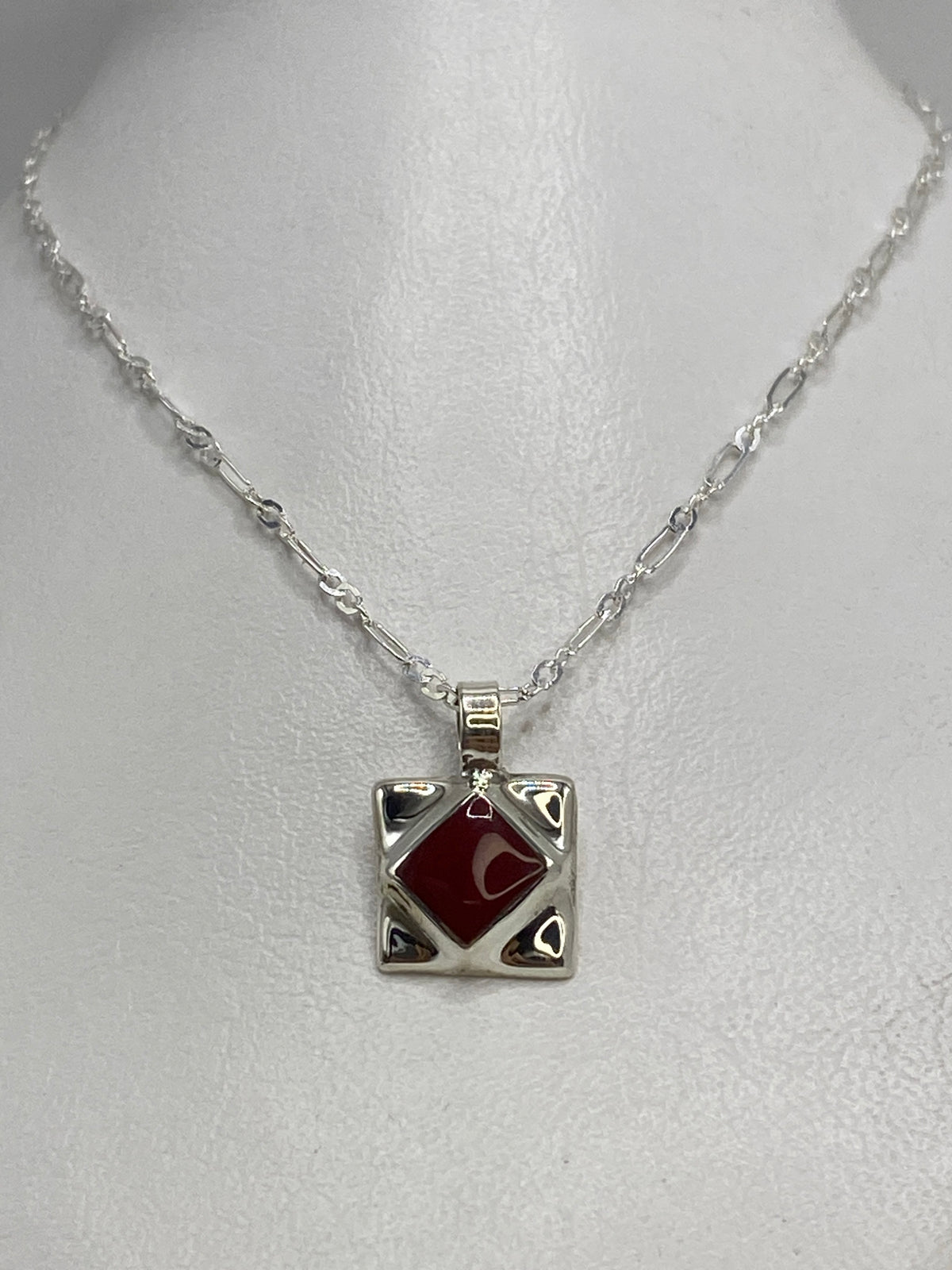 Detalle del dije compacto mostrando el engaste de piedra roja a mano