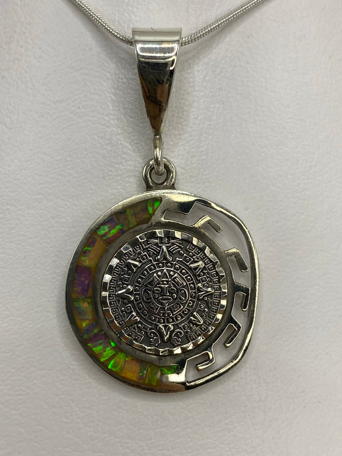 Dije del Calendario Azteca en plata 950 con ópalo de fuego multicolor colgando de una cadena plateada