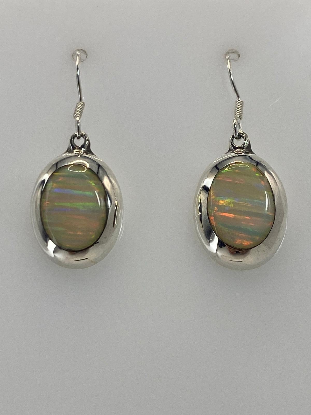 Aretes de ópalo mostrando el juego de luz naranja, rojo y verde dentro de la piedra