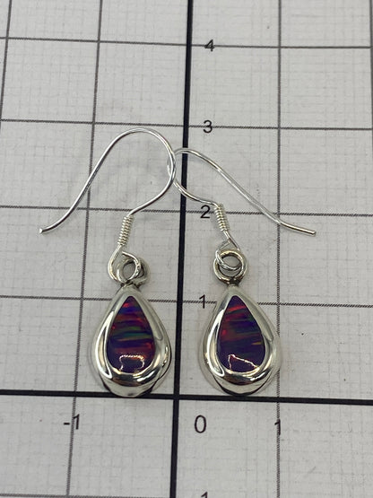Aretes de plata con ópalo morado en la mano, reflejos del fuego interno de la piedra