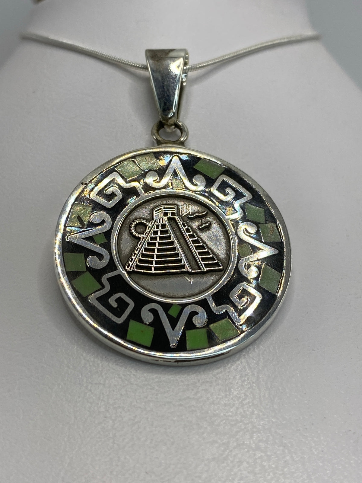 Detalle frontal del dije mostrando la pirámide de Chichén Itzá y motivos prehispánicos grabados
