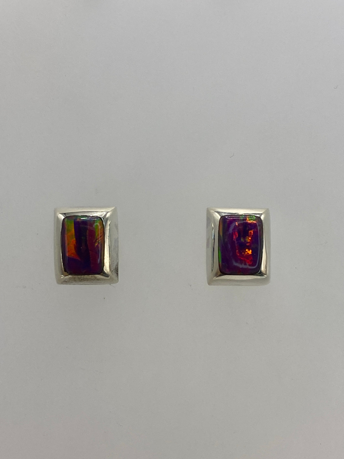 Aretes de plata con ópalo de fuego morado engastados a mano, sobre fondo blanco