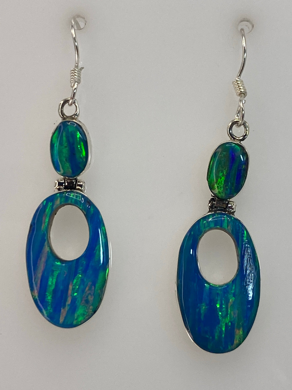 Par de aretes de plata con opalo de fuego azul de 3.8 cm colgando sobre fondo blanco