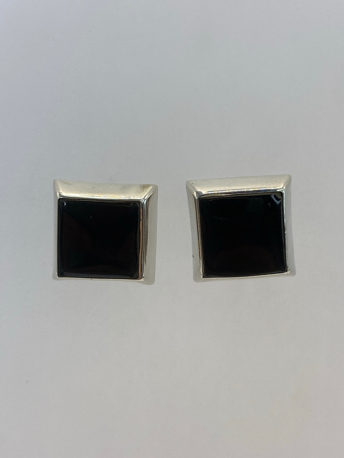 Par de aretes de plata 925 con piedra negra engastada, vistos de frente sobre fondo blanco