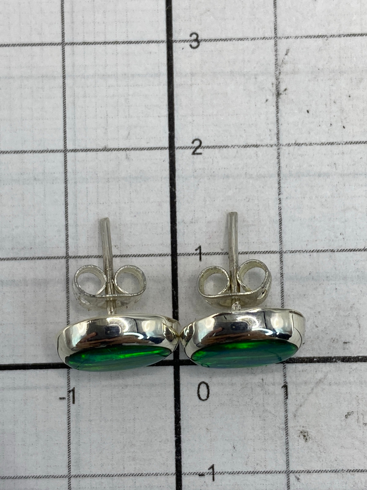 Aretes sobre paño neutro junto a regla de medida mostrando 1.3 cm