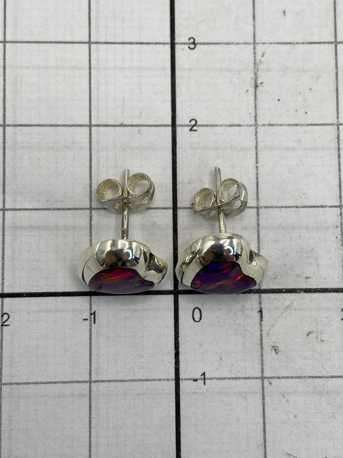 Aretes de ópalo fuego sobre fondo blanco junto a medida de escala