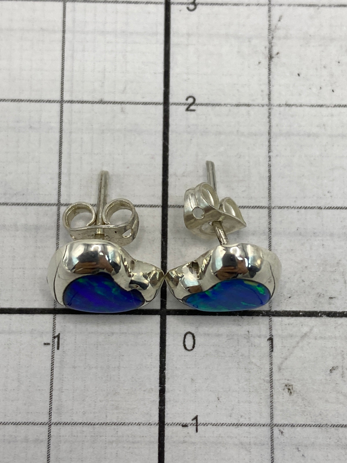Aretes de ópalo de fuego sobre medidor de tamaño, mostrando el largo de 1.3 cm