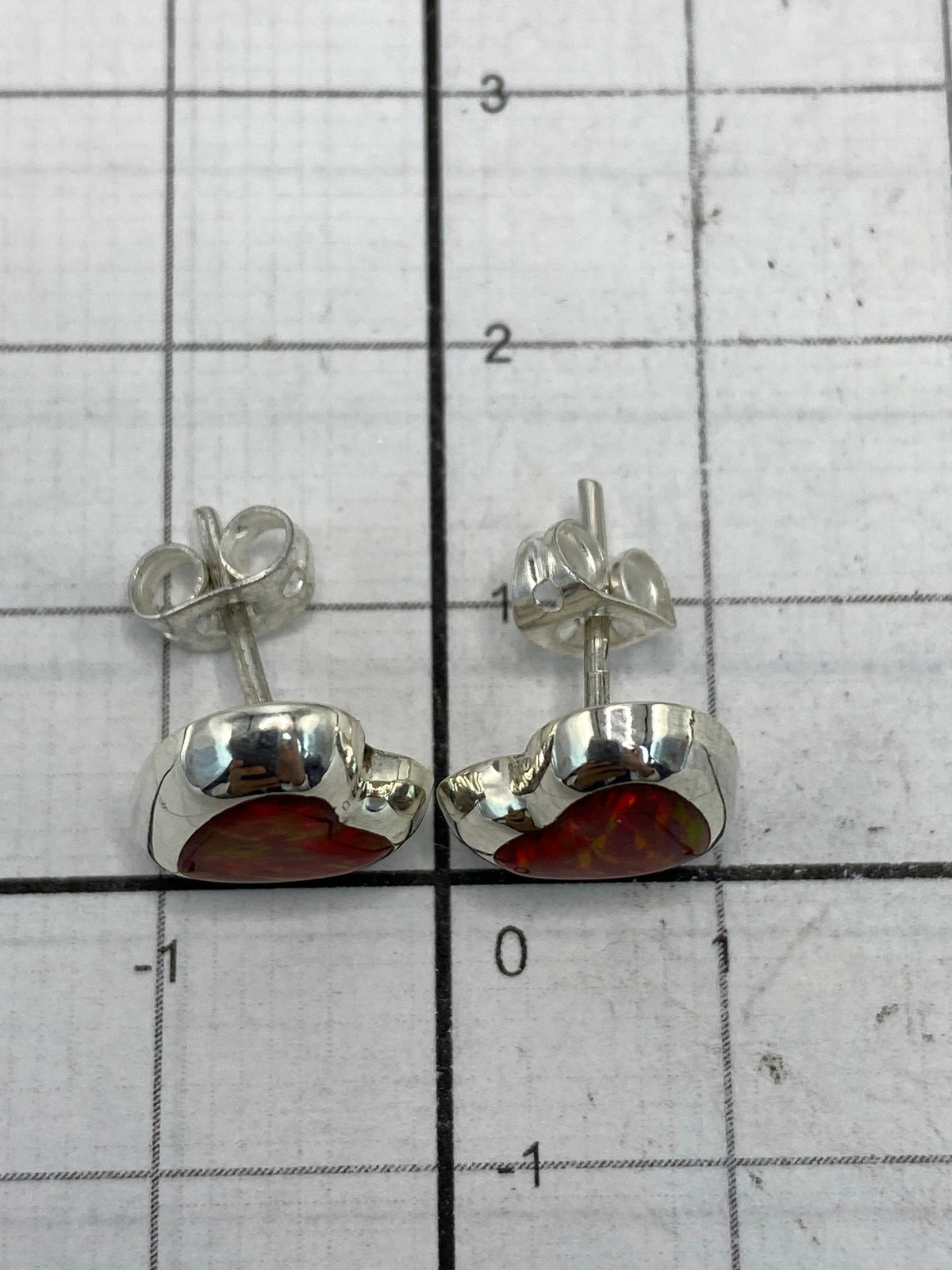 Aretes sobre regla de centímetros mostrando tamaño real de 1.3 cm