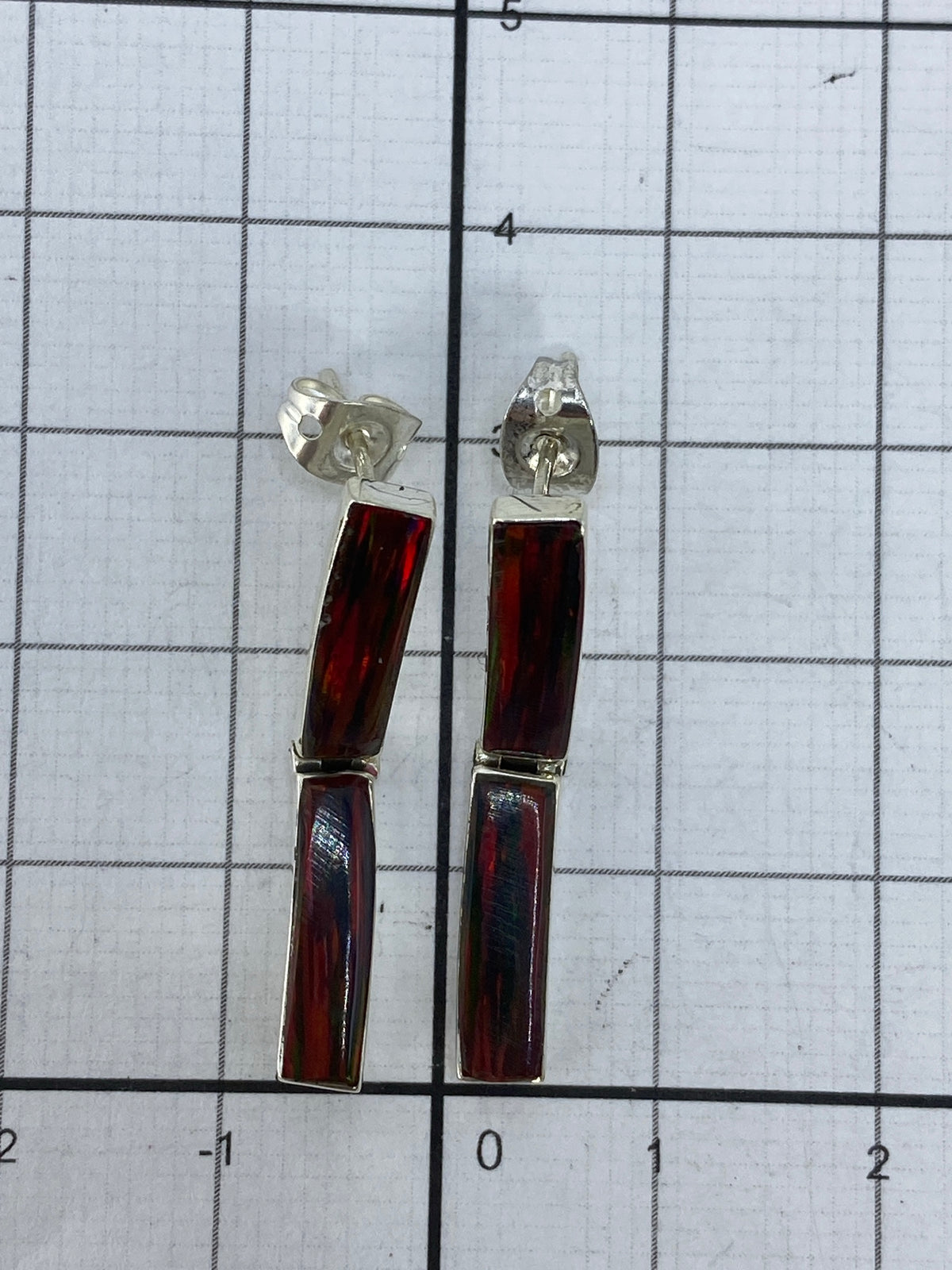 Aretes de plata con ópalo de fuego puestos, mostrando el juego de luz rojo y naranja