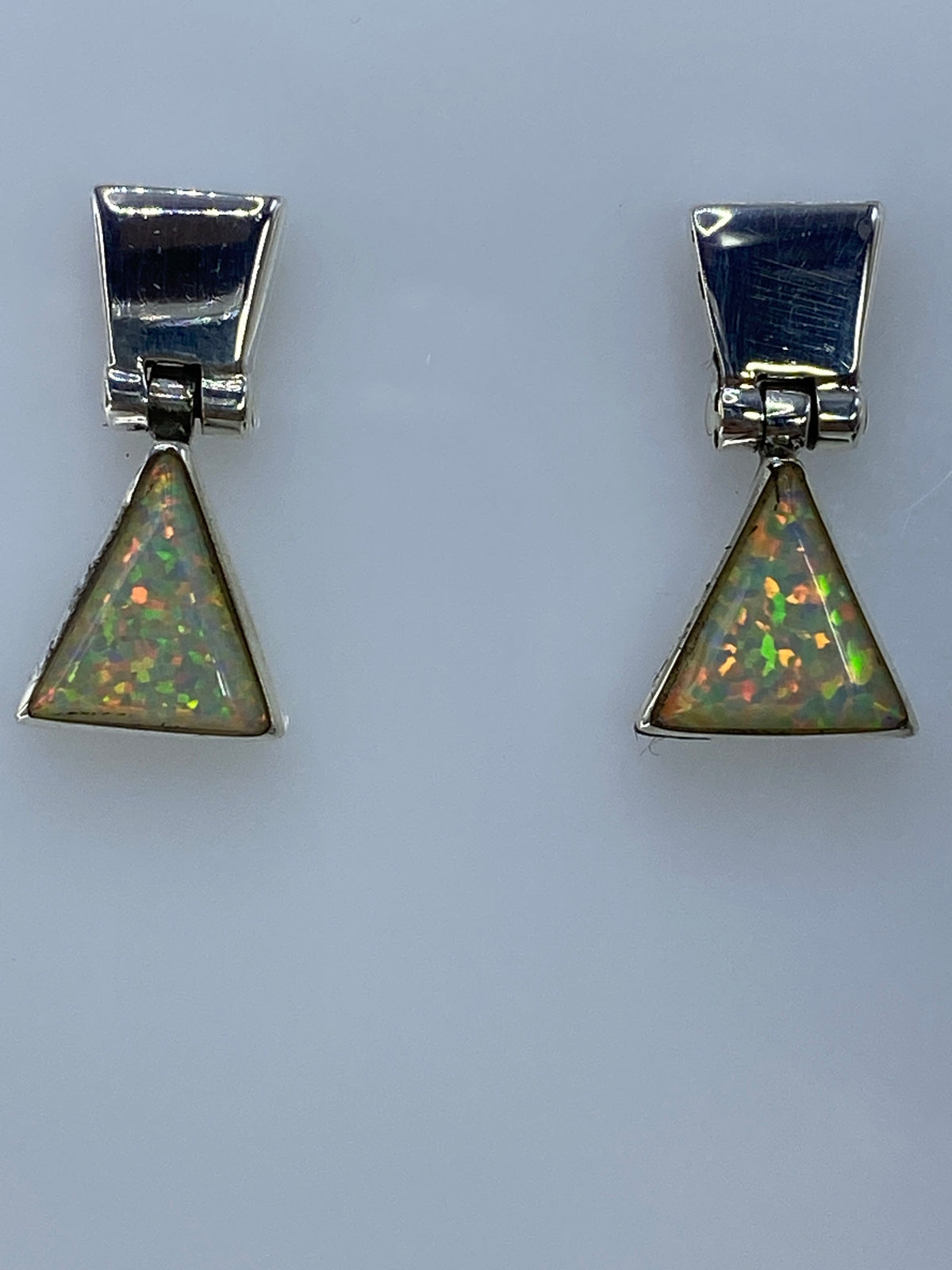 Aretes triangulares de plata brillante con piedra de fuego en fondo gris